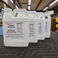Four 32 ounce white plastic jugs of Rosini's Furniture Preservative and Rejuvenator arranged in a row on a dark gray surface inside a warehouse workshop.