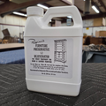 A white plastic bottle of Rosini's Furniture Preservative and Rejuvenator on a dark gray surface in a warehouse workshop.