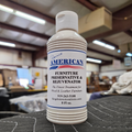An 8 fluid ounce bottle of Rosini's American Furniture Preservative and Rejuvenator on a dark gray surface with a blurred warehouse workshop in the background.